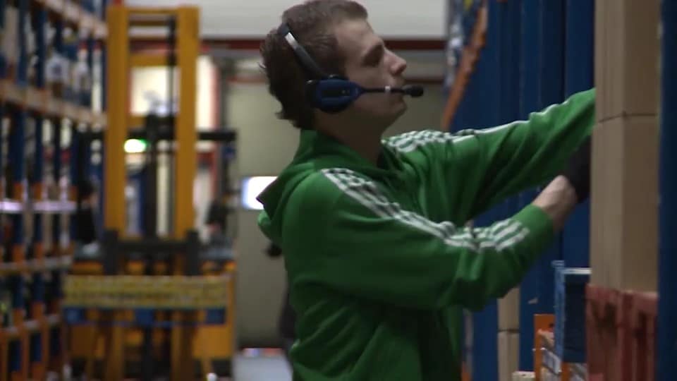 Warehouse worker from Coop with voice picking headset for voice control is picking an item in a distribution center